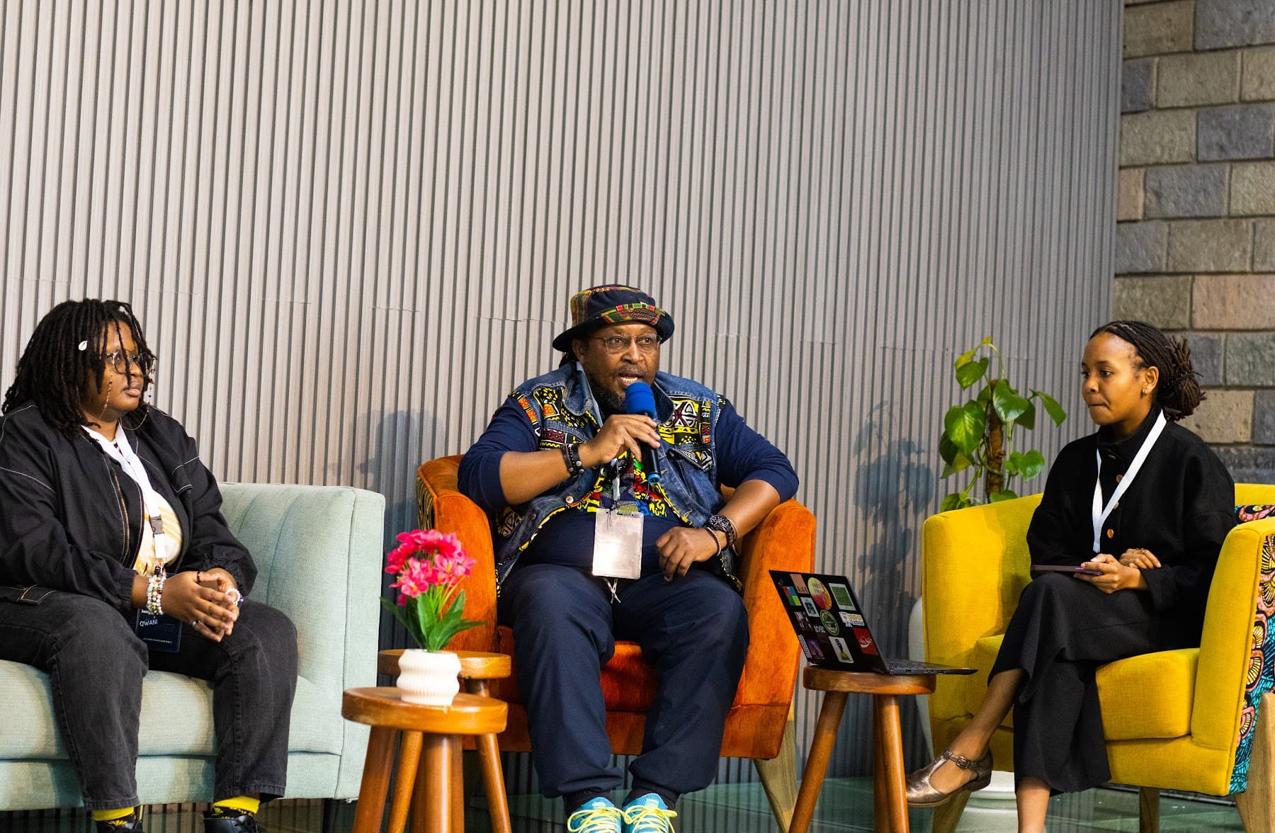 Three panellists in armchairs on stage, the centre speaker holding a microphone